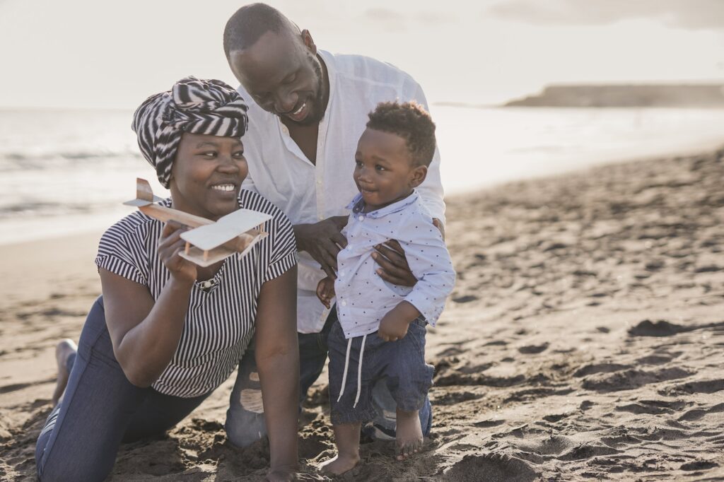 Happy african family having playful time on the beach - Family love - Parents and toddler outdoor