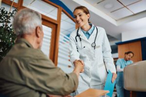 Happy doctor handshaking with her senior patient in waiting room at the clinic.