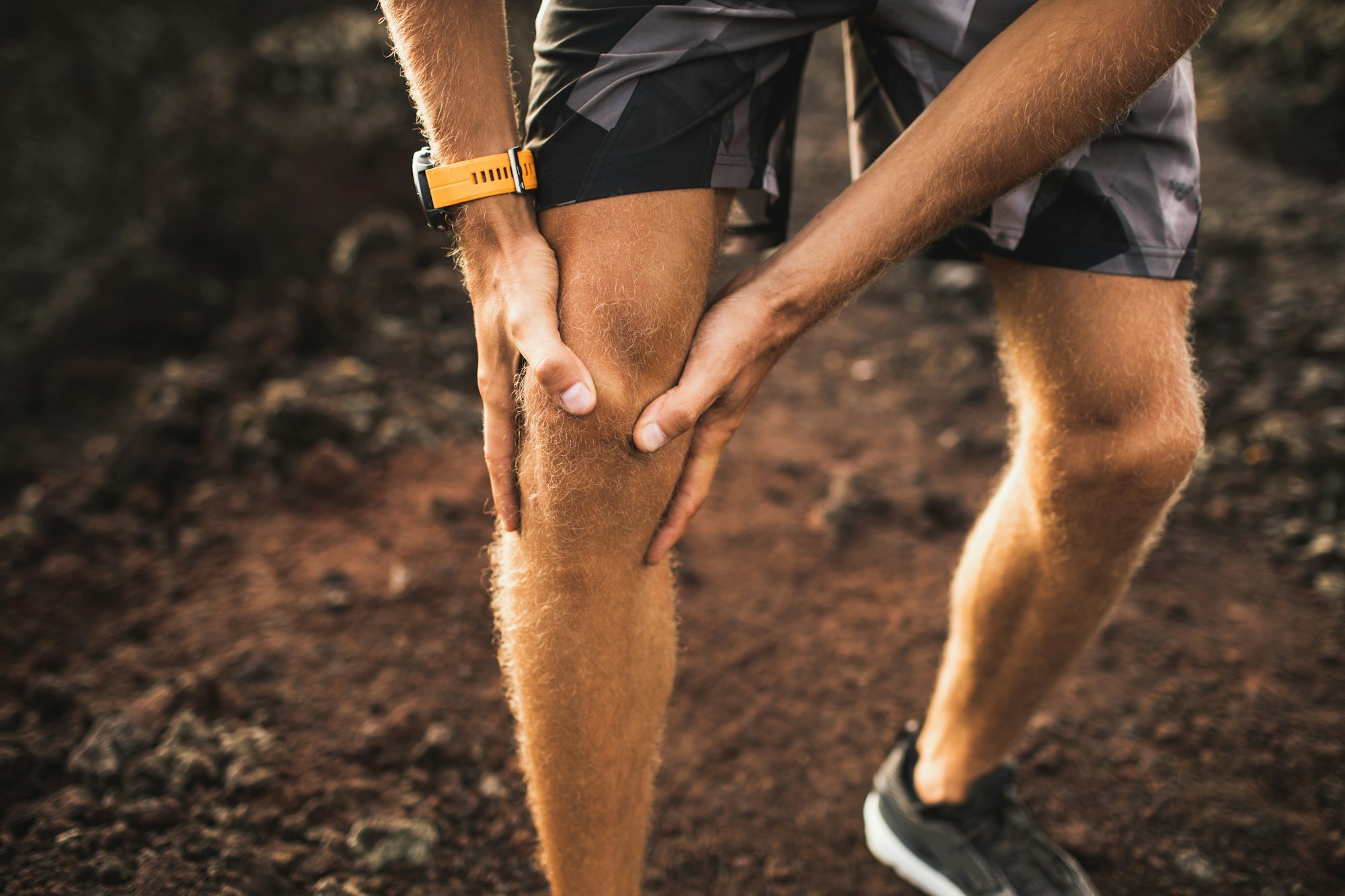 Knee injury on running outdoors. Man holding knee by hands close-up and suffering with pain
