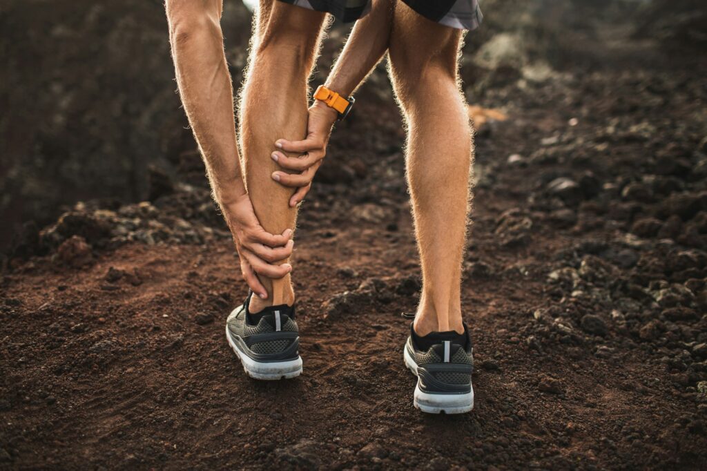 Male runner holding injured calf muscle and suffering with achilles tendon pain.