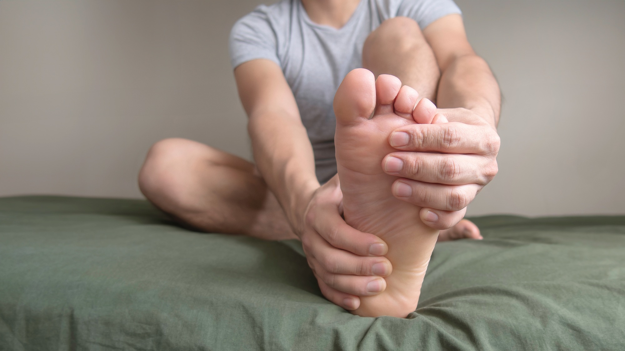 Person massaging their foot due to pain in the sole, arch and toes. Space for text on the left.