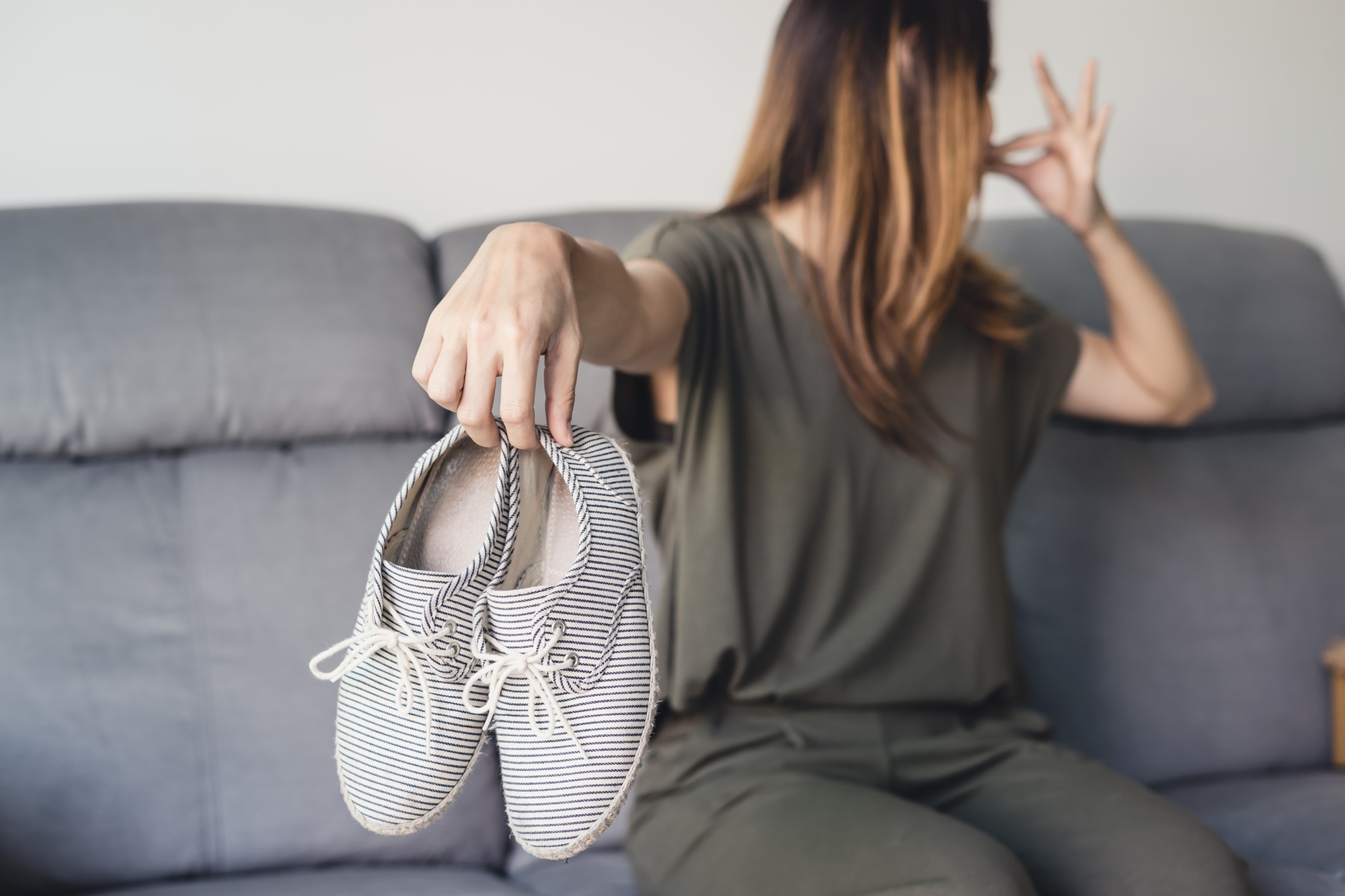 Young woman holding a pair of smelly shoes